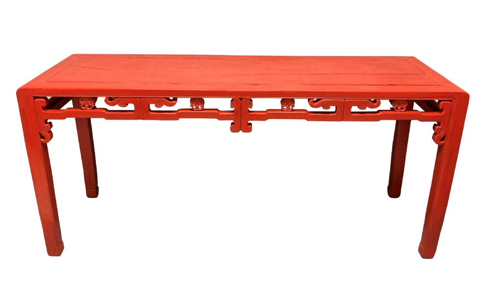 A 19th-century Chinese red lacquered console table featuring a long rectangular top and carved scroll aprons along the frame.