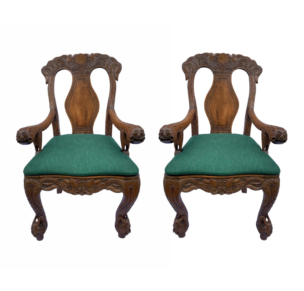 A pair of 19th-century carved teak Chinese armchairs featuring dragon motif armrests, detailed back splats, cabriole legs, and green upholstered seat cushions.
