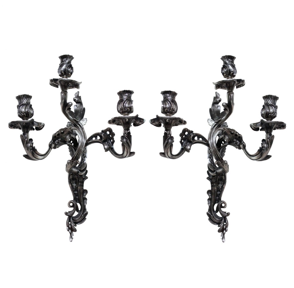 A pair of three-light silver-plated wall sconces with ornate Rococo scrolling branches and leaf ornamentation.