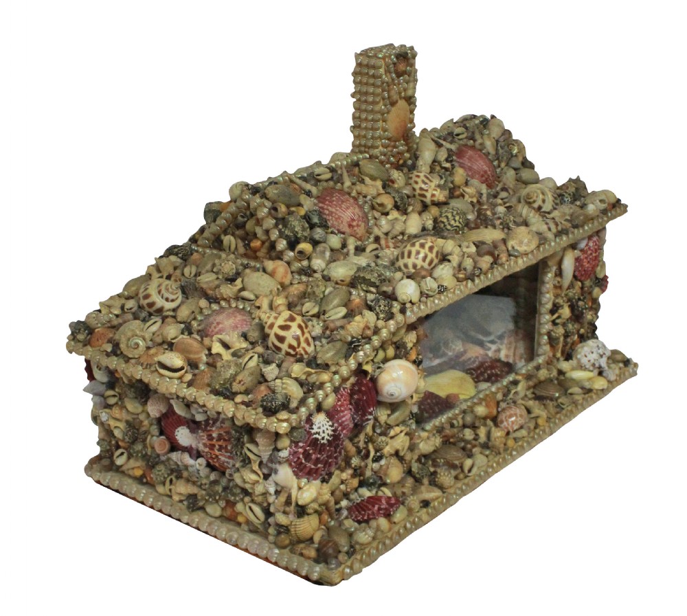 A miniature cottage-shaped decorative object encrusted with various small natural seashells and featuring a central open recess and a shell-covered chimney. View II