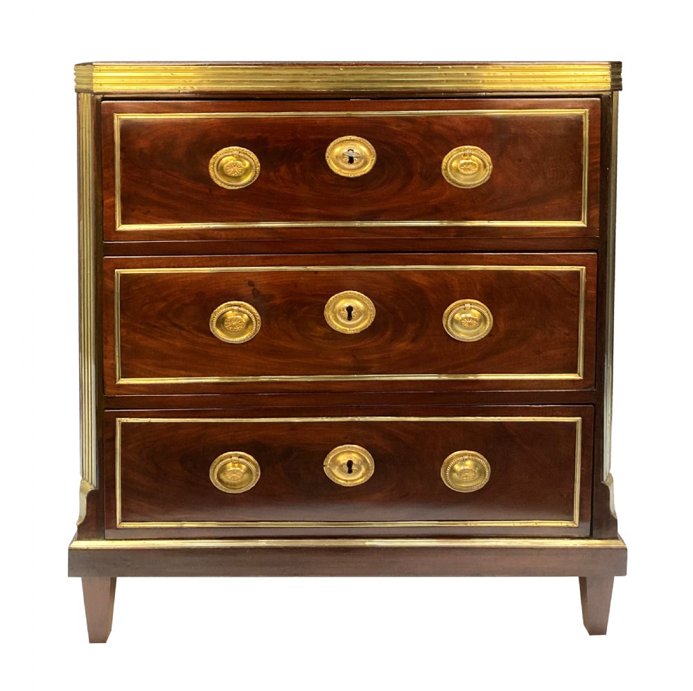 An early nineteenth-century Russian mahogany commode with three drawers decorated with brass inlay borders, circular brass handles, central escutcheons, and fluted brass side pilasters.