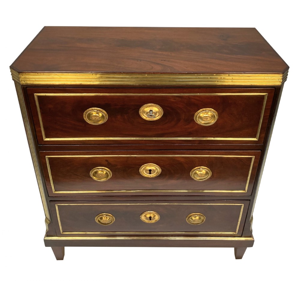 An early nineteenth-century Russian mahogany commode with three drawers decorated with brass inlay borders, circular brass handles, central escutcheons, and fluted brass side pilasters. View VI