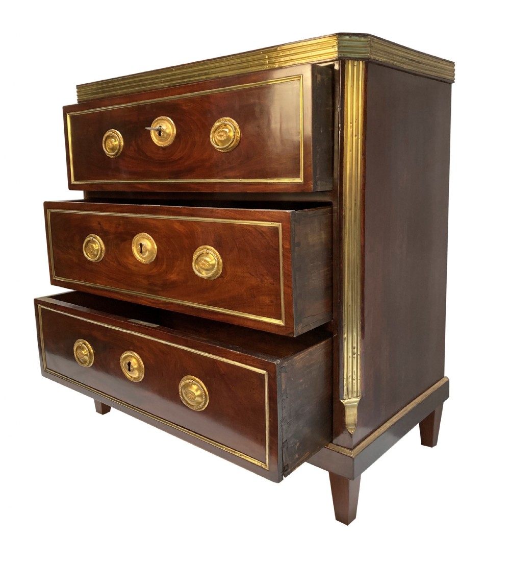 An early nineteenth-century Russian mahogany commode with three drawers decorated with brass inlay borders, circular brass handles, central escutcheons, and fluted brass side pilasters. View VII