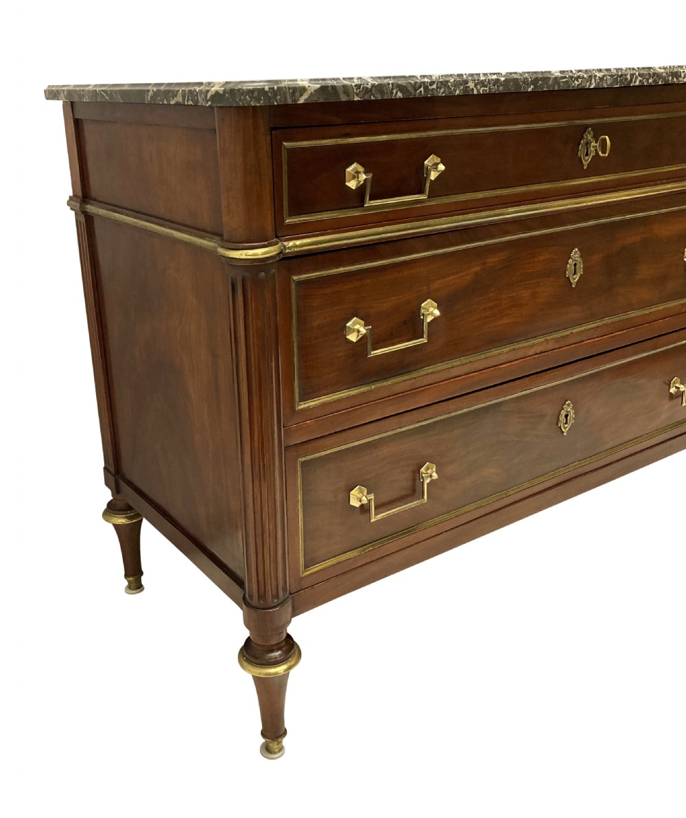 A French Directoire mahogany commode featuring three long drawers with brass mounts, fluted corner pilasters, and a grey marble top. View III