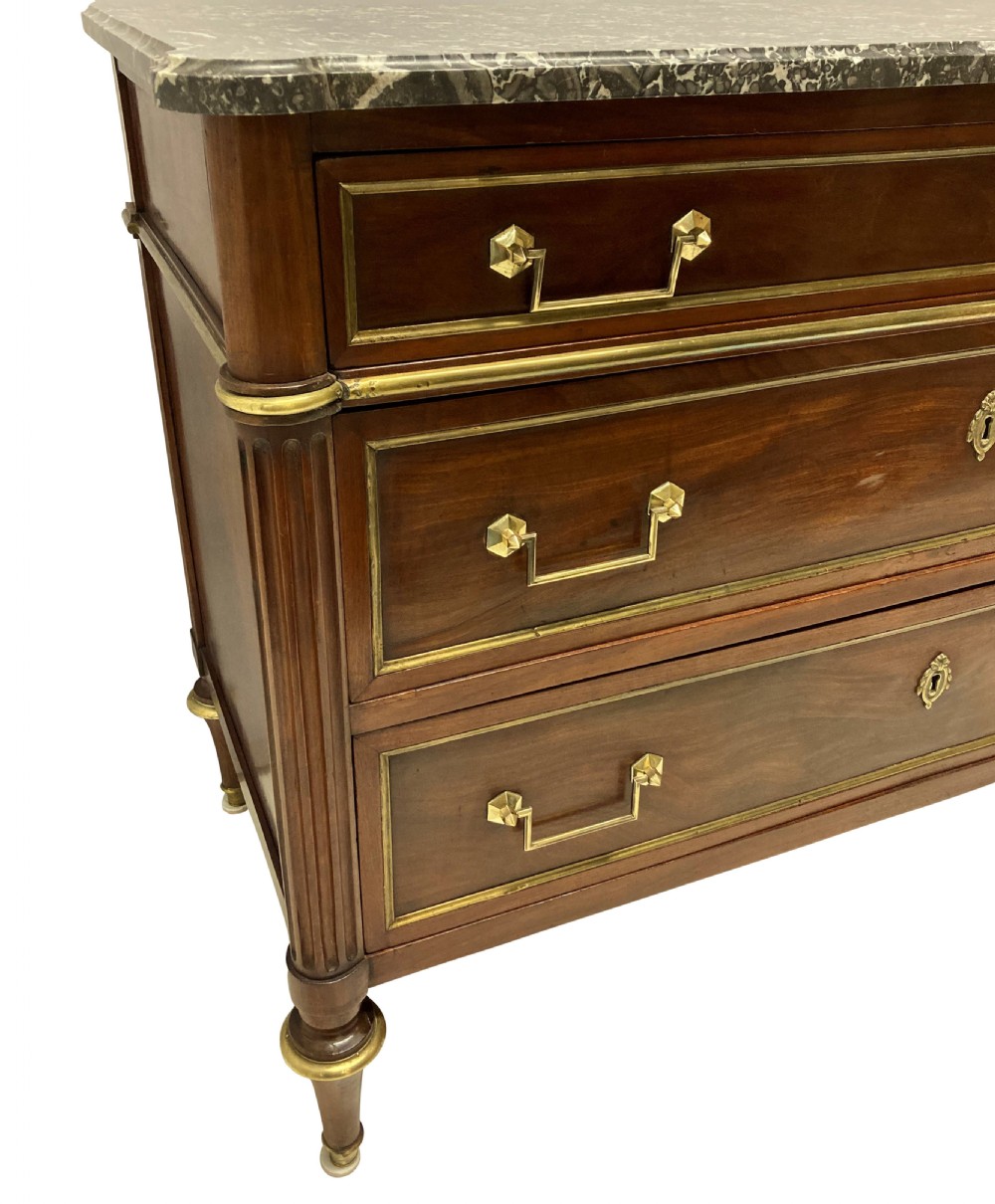 A French Directoire mahogany commode featuring three long drawers with brass mounts, fluted corner pilasters, and a grey marble top. View V