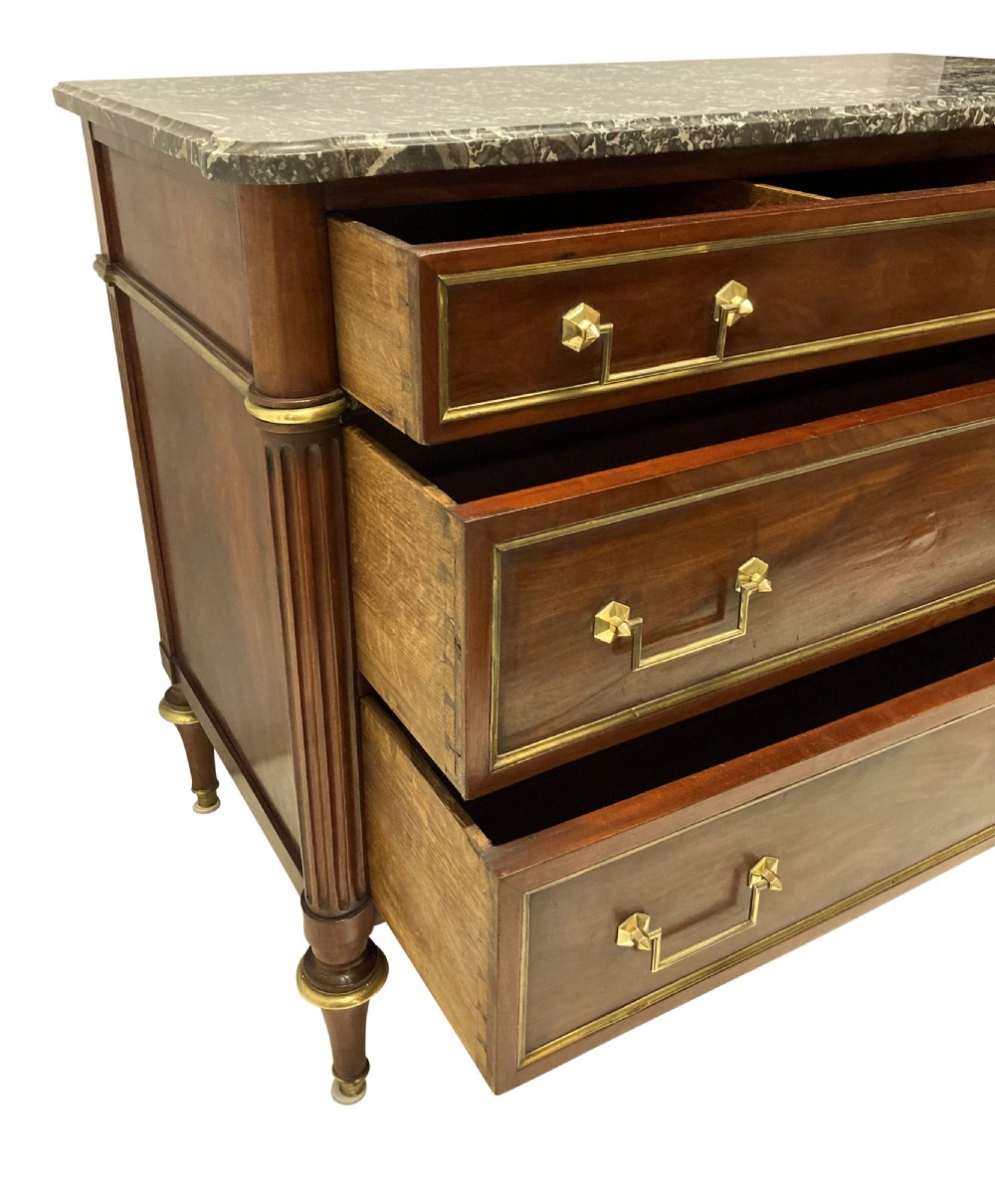 A French Directoire mahogany commode featuring three long drawers with brass mounts, fluted corner pilasters, and a grey marble top. View IX