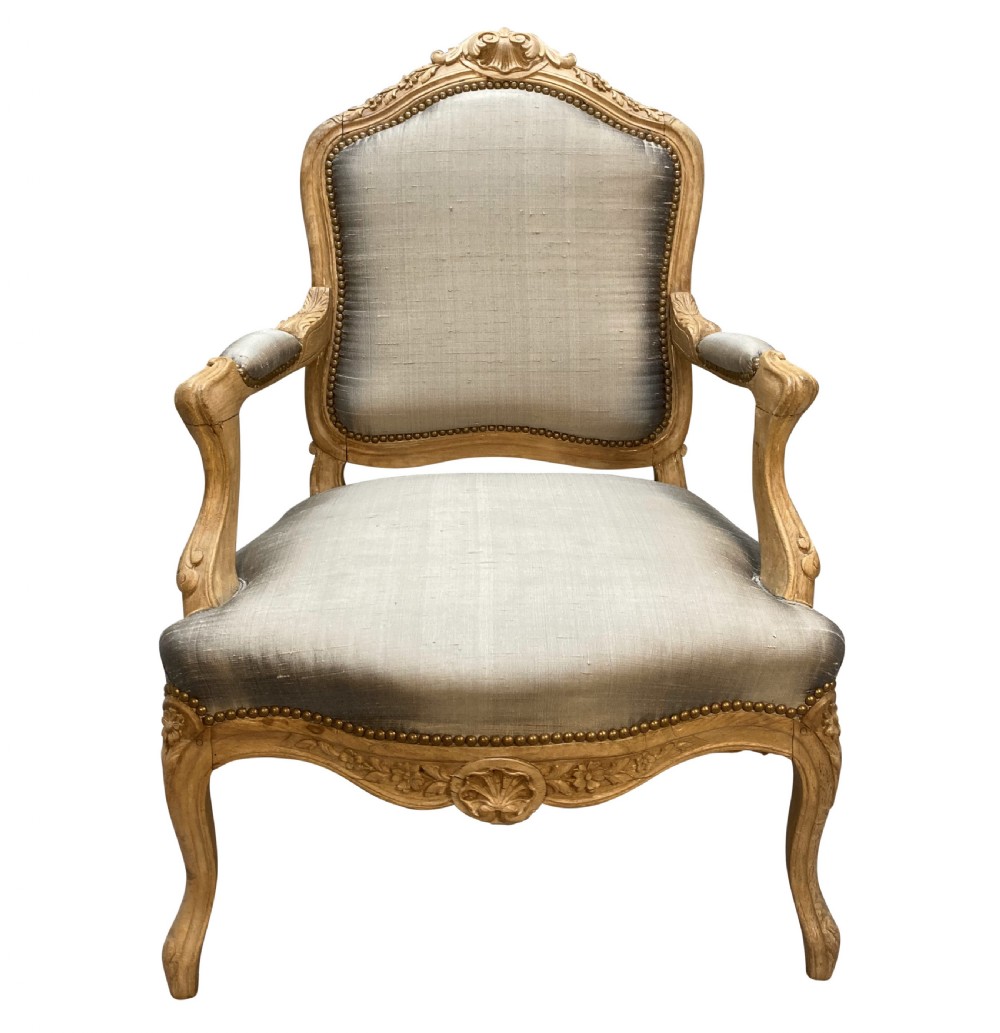A Louis XV style armchair featuring a carved bleached fruitwood frame with cabriole legs and grey silk upholstery secured with brass studs. View II