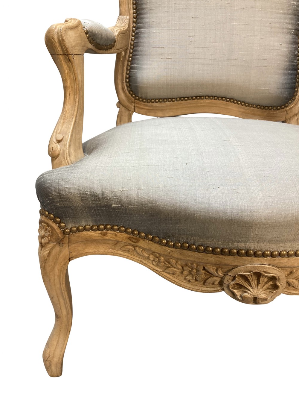 A Louis XV style armchair featuring a carved bleached fruitwood frame with cabriole legs and grey silk upholstery secured with brass studs. View VI