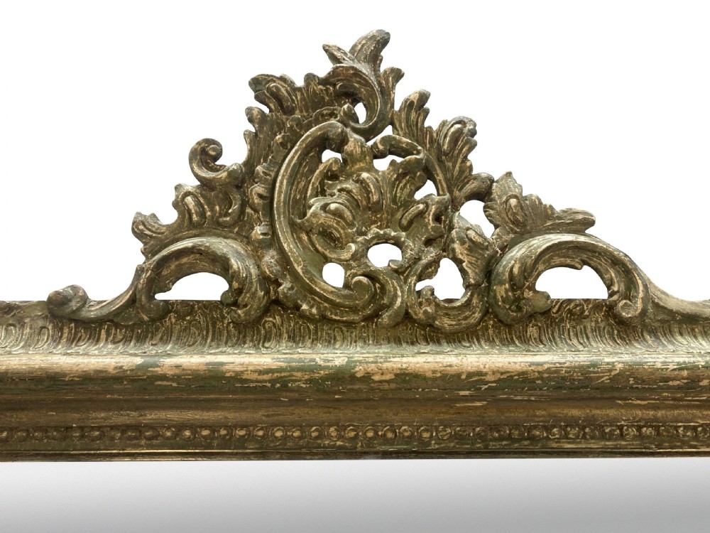 An arched Louis XV style rectangular overmantel mirror featuring a carved ornate scroll crest and a weathered green and gilded frame. View V
