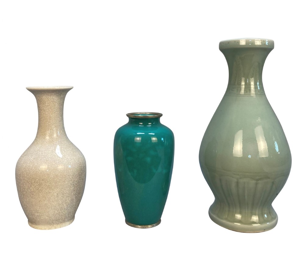 A trio of Japanese ceramic vases featuring a cream crackle-glazed vase, a small turquoise enamel vase with metal mounts, and a tall pale green celadon vase with carved lotus motifs.