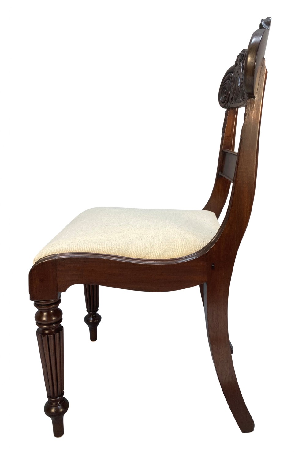 A set of four William IV Anglo-Indian dark wood dining chairs featuring carved scroll top rails, fluted turned front legs, and cream fabric seats. View IV