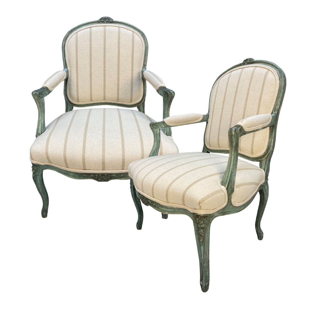 A pair of Louis XV style armchairs featuring distressed green painted frames, carved floral accents, cabriole legs, and neutral striped upholstery.