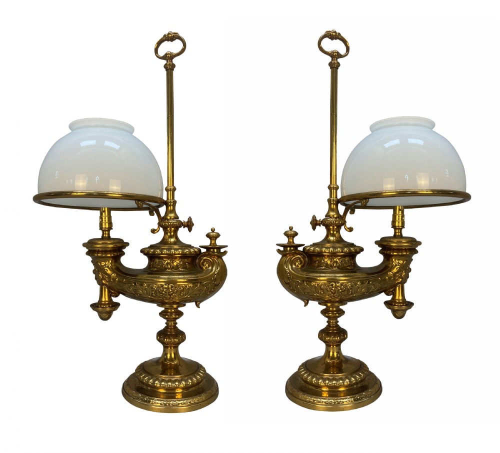 A pair of ornate 19th-century brass desk lamps featuring elaborate cast detail, tall central adjustment poles with ring finials, and white domed glass shades.