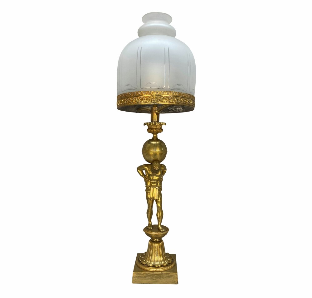 An English Regency gilt-bronze table lamp featuring a figure of Atlas supporting a sphere beneath a frosted glass dome shade.