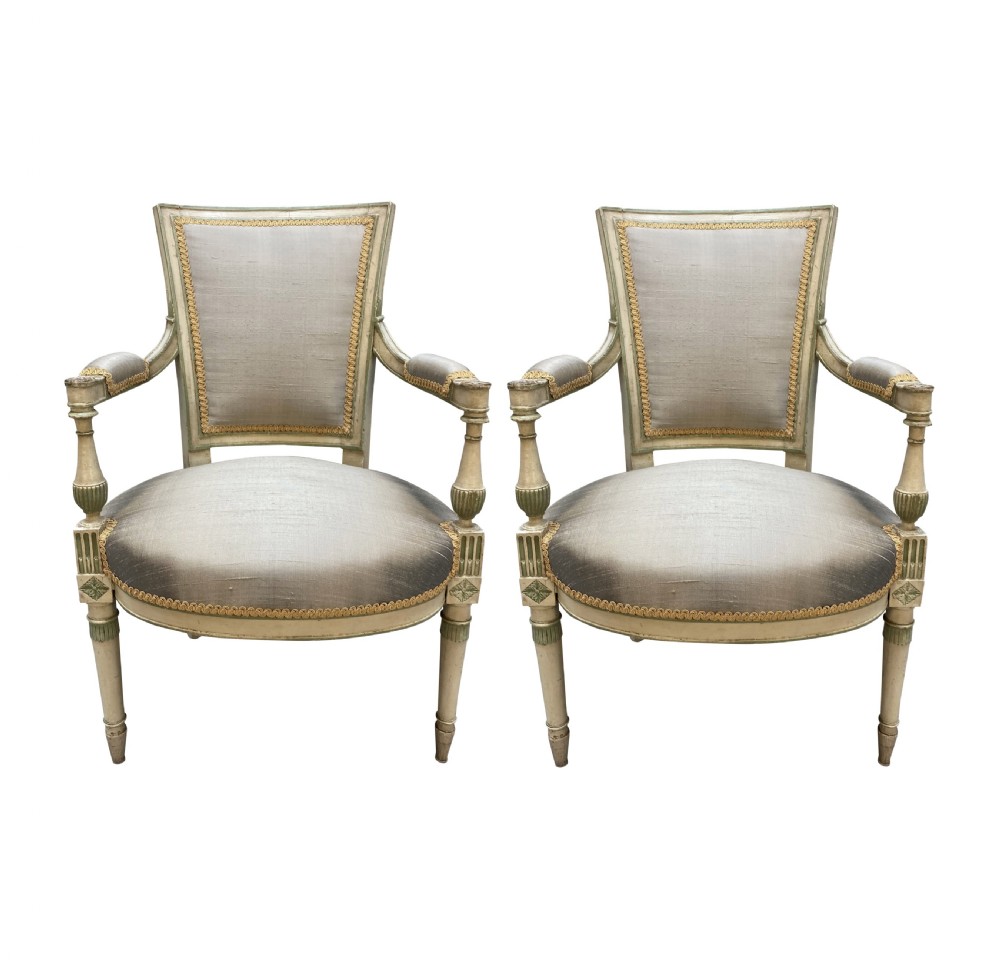 A pair of French Directoire style painted armchairs with grey silk upholstery, fluted legs, and cream-painted frames.