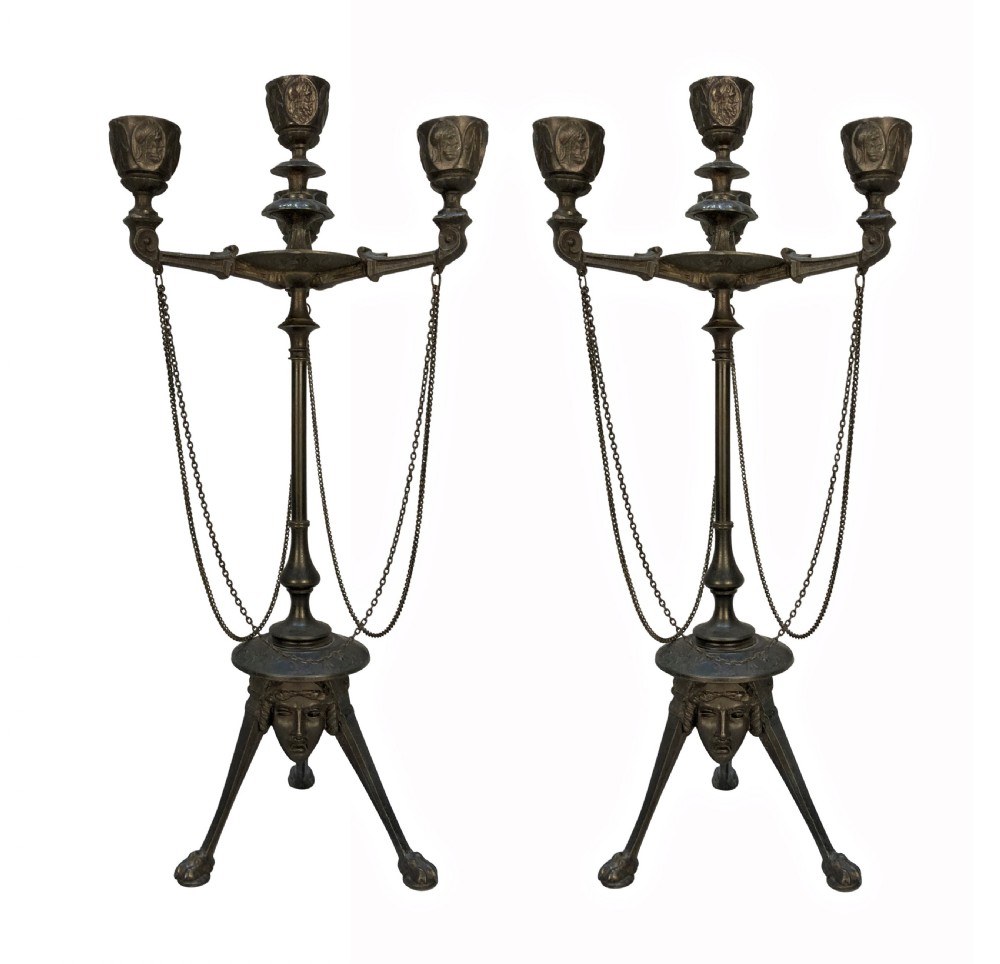 A pair of 19th-century dark bronze three-light candelabra with draped metal chains, classical face masks, and tripod bases ending in claw feet.