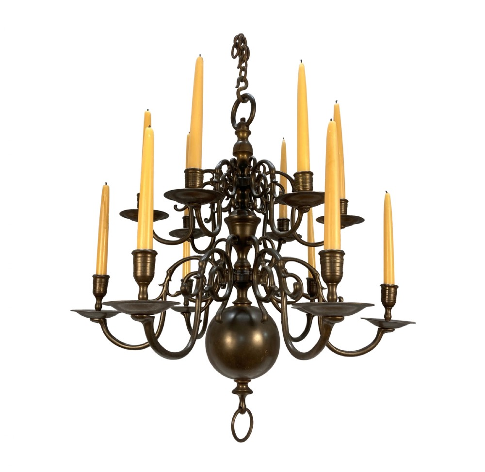 A nineteenth-century multi-tiered bronze chandelier in the Dutch taste featuring scrolling S-curved arms, cylindrical candle nozzles with drip pans, and a central baluster stem terminating in a heavy spherical drop.