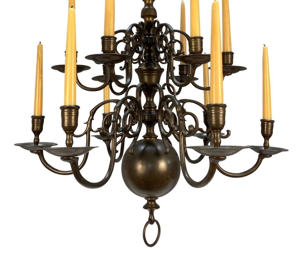 A nineteenth-century multi-tiered bronze chandelier in the Dutch taste featuring scrolling S-curved arms, cylindrical candle nozzles with drip pans, and a central baluster stem terminating in a heavy spherical drop. View II