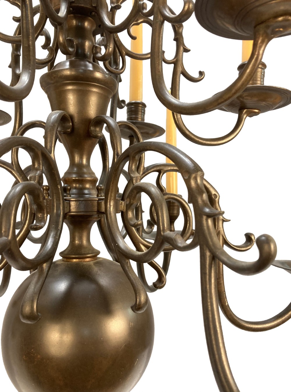 A nineteenth-century multi-tiered bronze chandelier in the Dutch taste featuring scrolling S-curved arms, cylindrical candle nozzles with drip pans, and a central baluster stem terminating in a heavy spherical drop. View VII