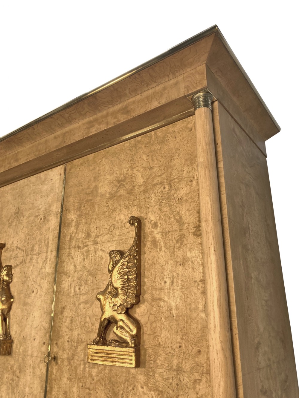 A large two-door Swedish Empire Revival cupboard crafted in light birds eye maple wood featuring gilt winged sphinx mounts and brass trim. View VI