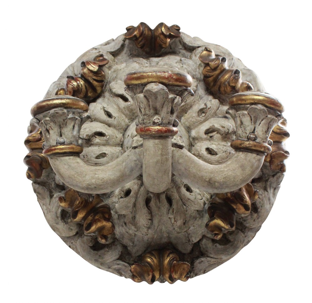 A 19th-century carved wooden three-branch wall sconce with detailed acanthus leaf decoration, distressed grey paint, and gilded accents.