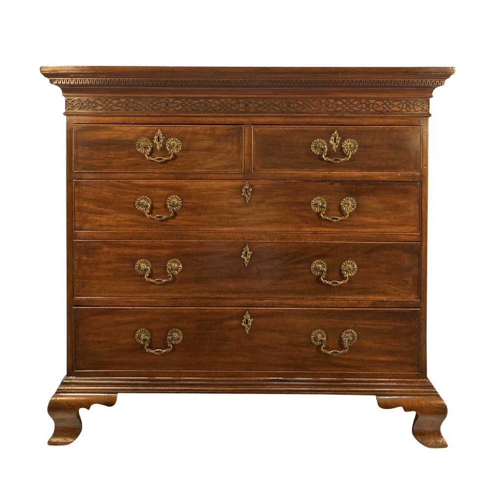An English Chippendale style mahogany chest of drawers featuring ornate brass handles, a carved fretwork frieze, and bracket feet.