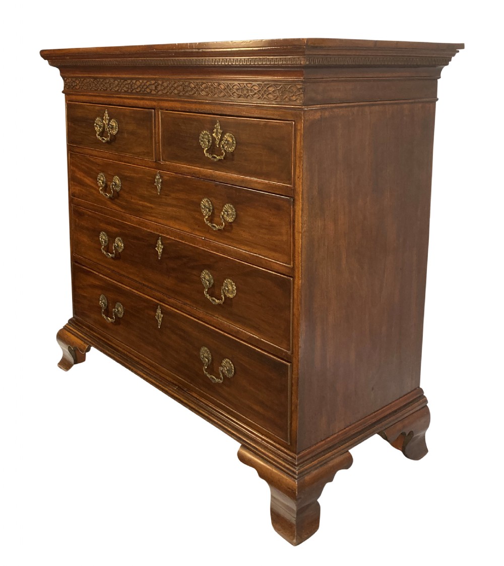 An English Chippendale style mahogany chest of drawers featuring ornate brass handles, a carved fretwork frieze, and bracket feet. View II