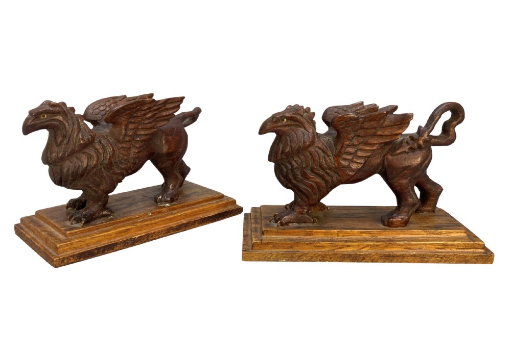 A pair of hand-carved wooden griffin statues facing each other, each mounted on a stepped rectangular plinth. View II