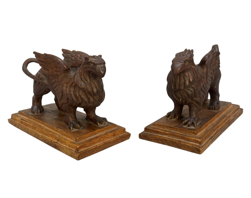 A pair of hand-carved wooden griffin statues facing each other, each mounted on a stepped rectangular plinth. View III
