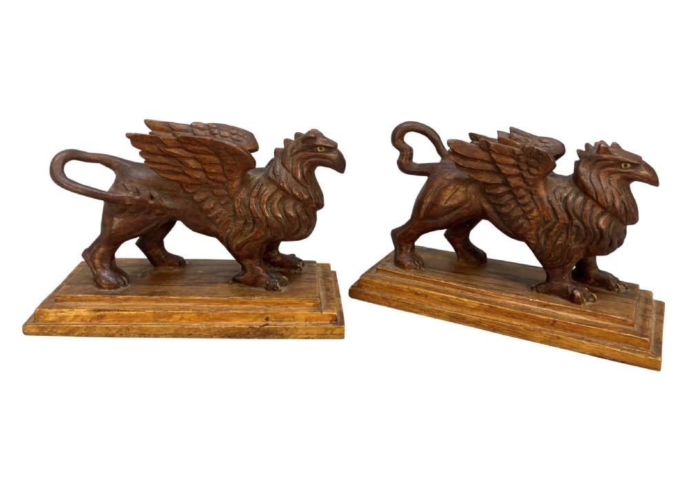 A pair of hand-carved wooden griffin statues facing each other, each mounted on a stepped rectangular plinth. View IV