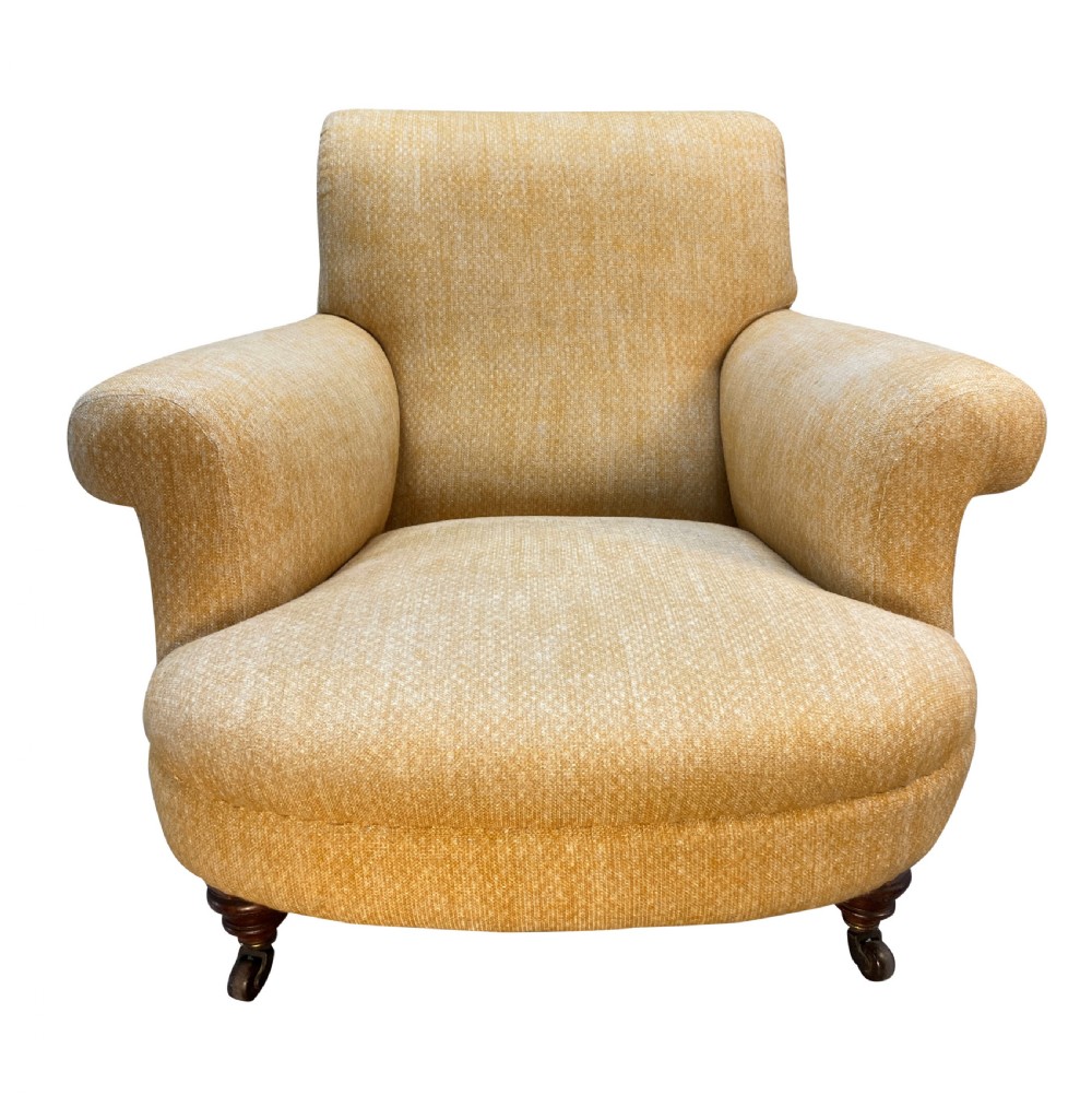 A low-slung Howard style club armchair upholstered in yellow textured fabric with turned wood front legs on castors. View II