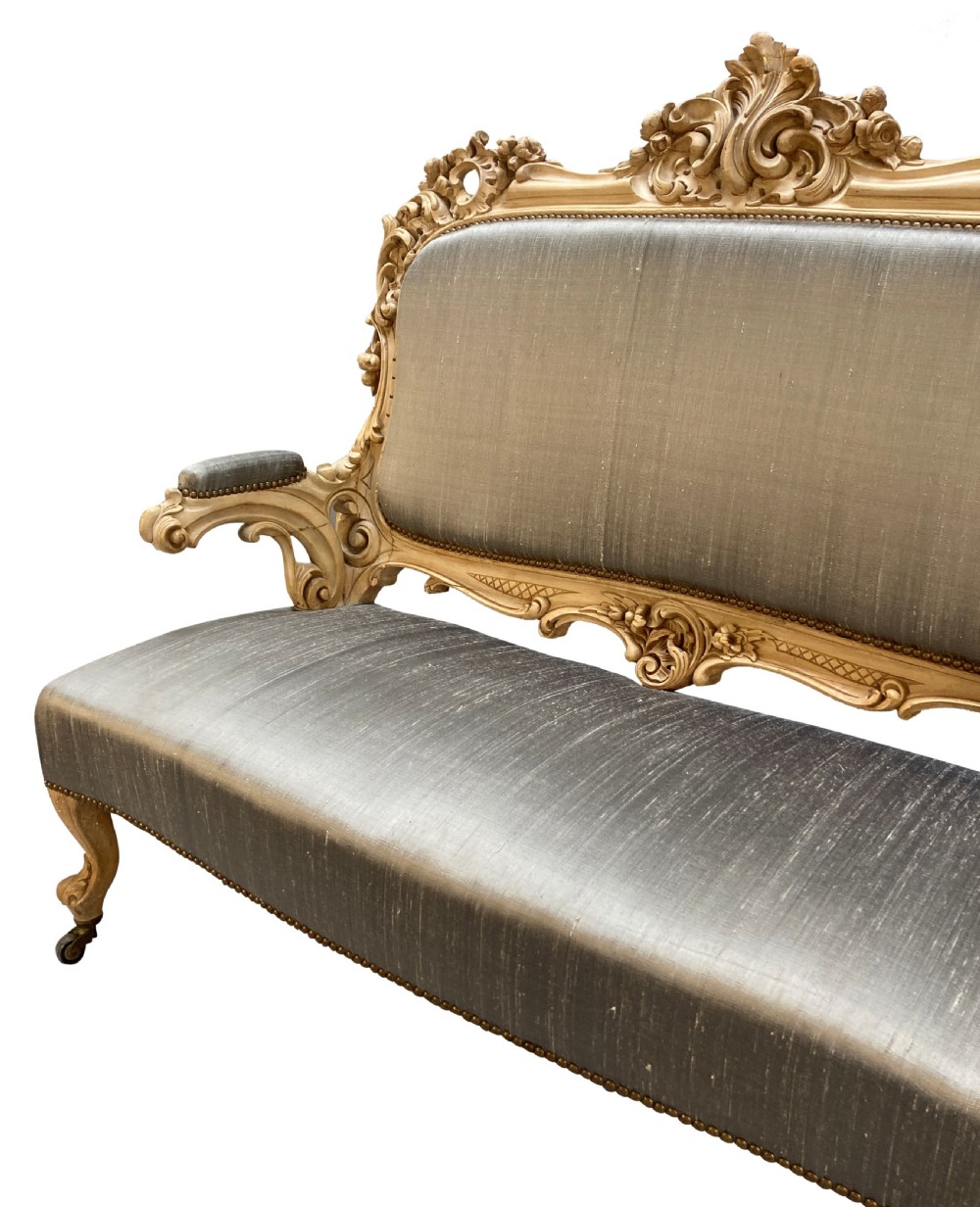 An early nineteenth-century German Rococo style upholstered settee with an elaborately carved crest rail, cabriole legs on castors, and silver-grey silk fabric seat and back. View II