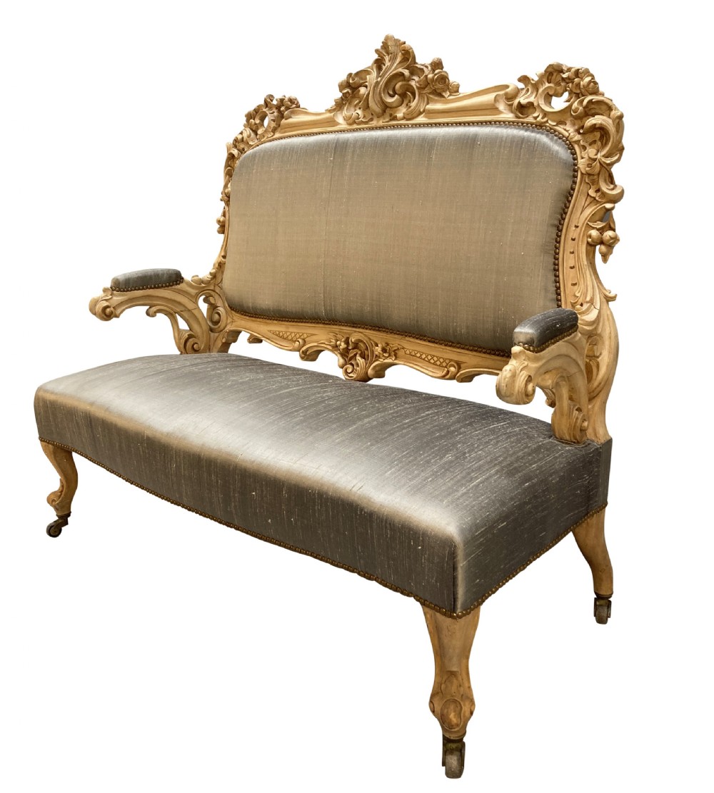 An early nineteenth-century German Rococo style upholstered settee with an elaborately carved crest rail, cabriole legs on castors, and silver-grey silk fabric seat and back. View III