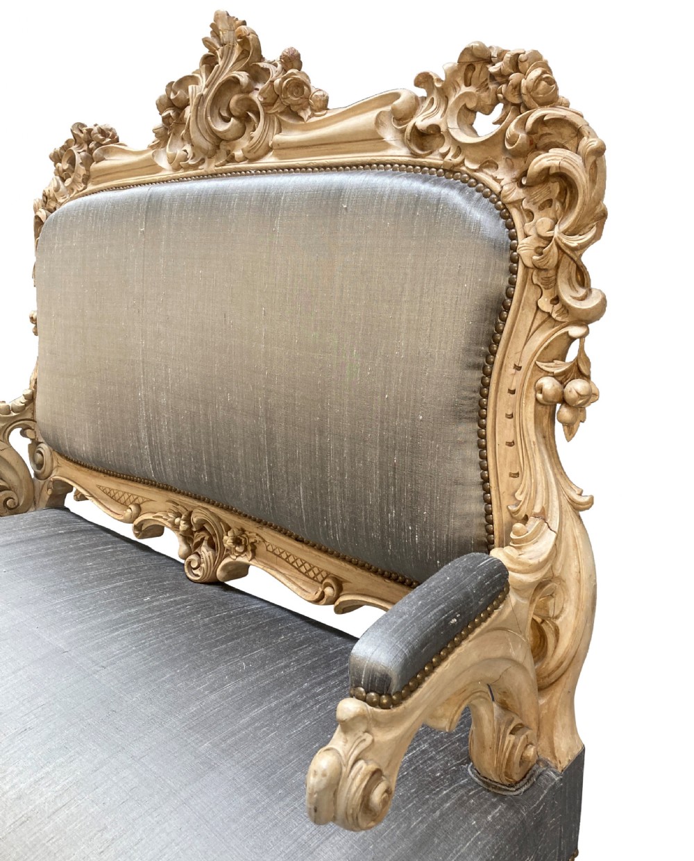 An early nineteenth-century German Rococo style upholstered settee with an elaborately carved crest rail, cabriole legs on castors, and silver-grey silk fabric seat and back. View V