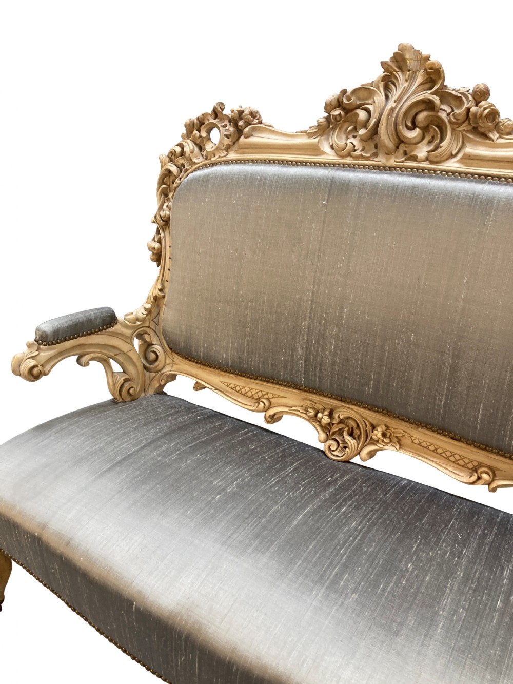 An early nineteenth-century German Rococo style upholstered settee with an elaborately carved crest rail, cabriole legs on castors, and silver-grey silk fabric seat and back. View VI