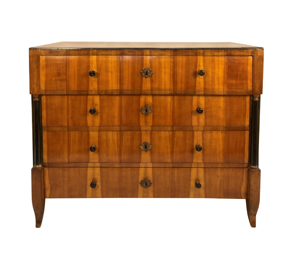 An early nineteenth-century Biedermeier chest of four drawers crafted from figured timber veneer, flanked by ebonised side columns and supported by tapered front legs.