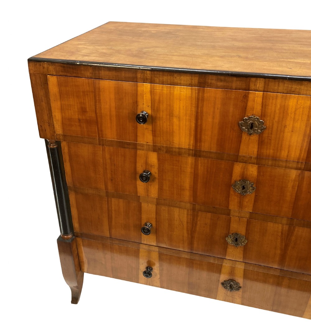 An early nineteenth-century Biedermeier chest of four drawers crafted from figured timber veneer, flanked by ebonised side columns and supported by tapered front legs. View V