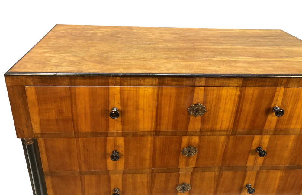 An early nineteenth-century Biedermeier chest of four drawers crafted from figured timber veneer, flanked by ebonised side columns and supported by tapered front legs. View VI