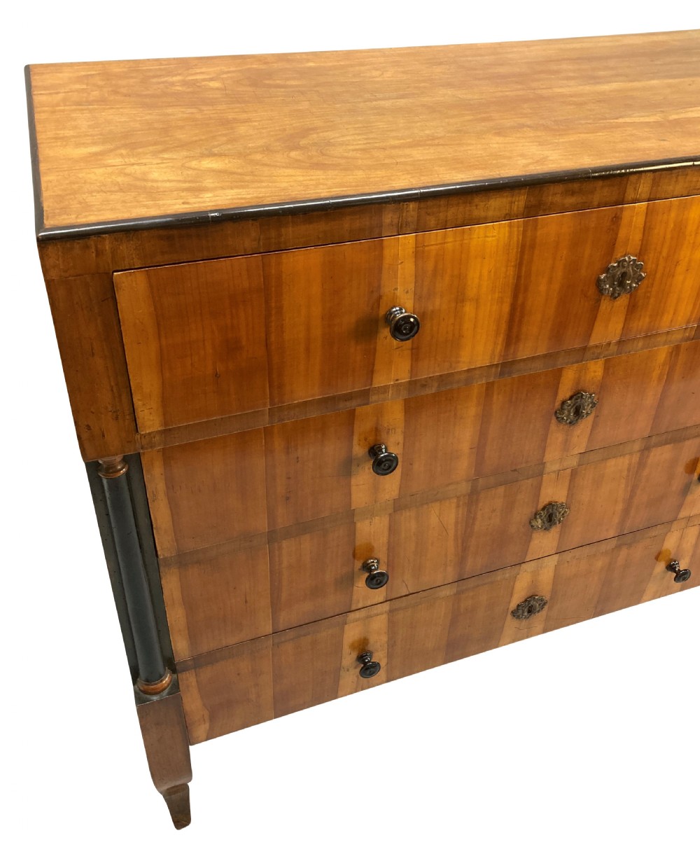 An early nineteenth-century Biedermeier chest of four drawers crafted from figured timber veneer, flanked by ebonised side columns and supported by tapered front legs. View VII