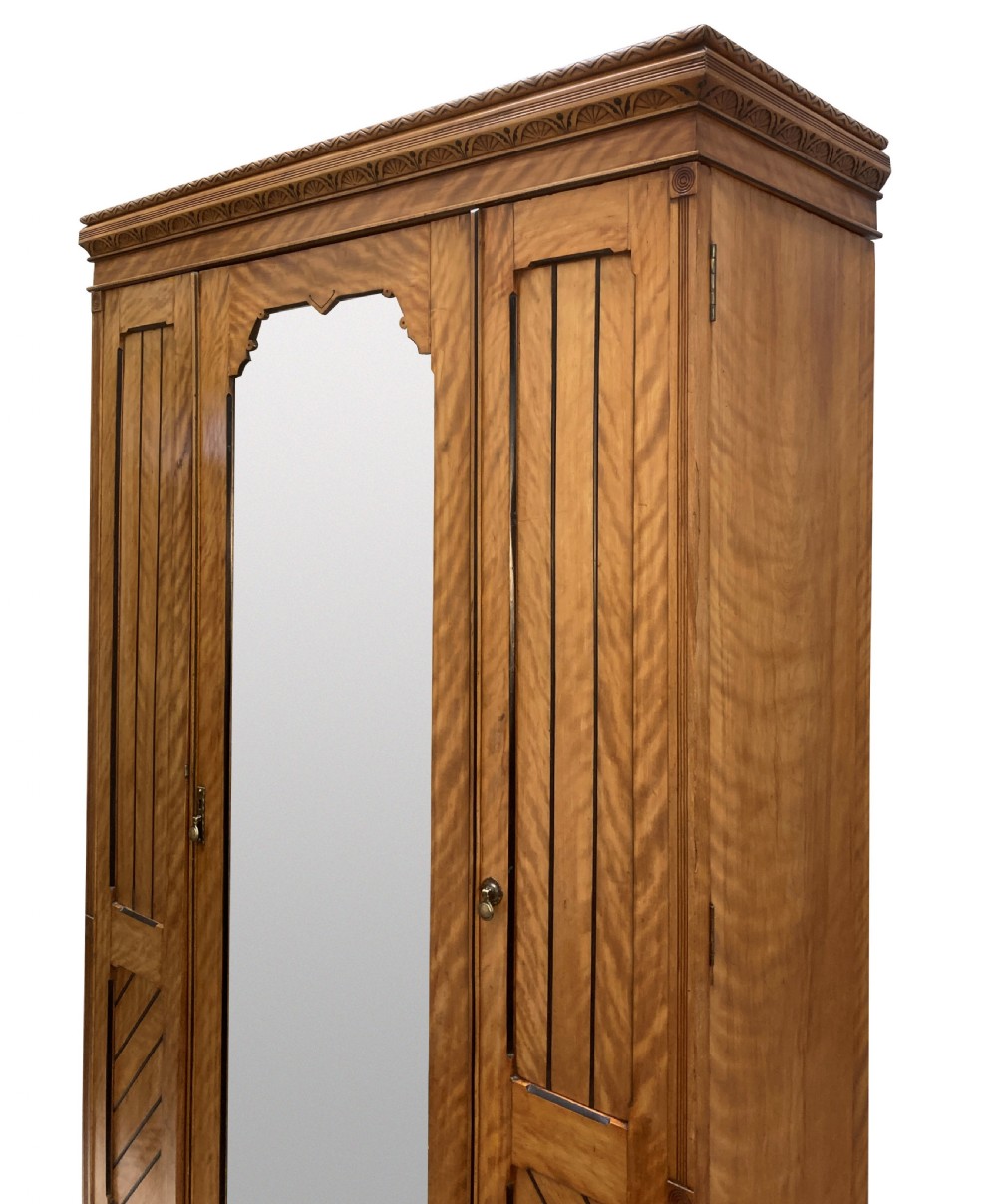 An Aesthetic Movement satin birch wardrobe featuring a central mirrored door flanked by geometric panelled side doors and a carved frieze. View III