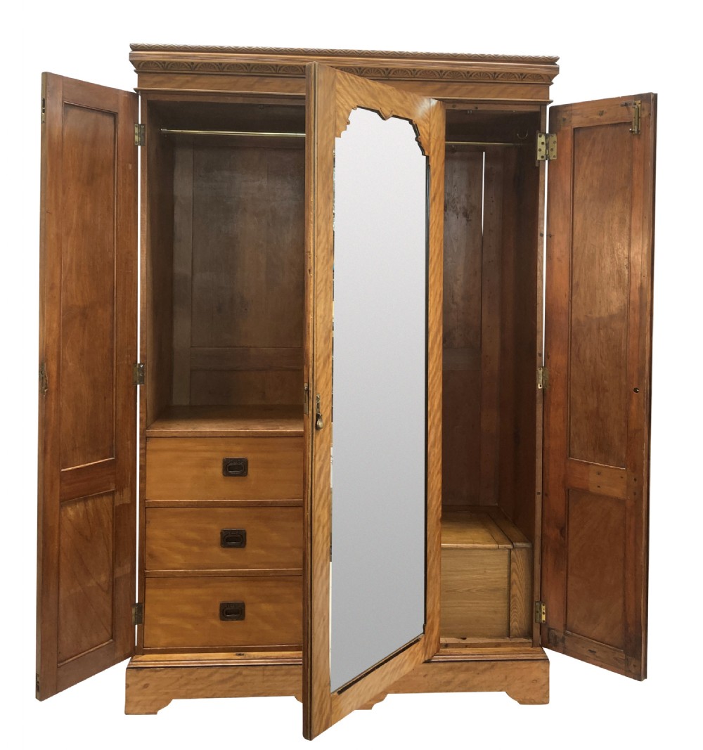 An Aesthetic Movement satin birch wardrobe featuring a central mirrored door flanked by geometric panelled side doors and a carved frieze. View V