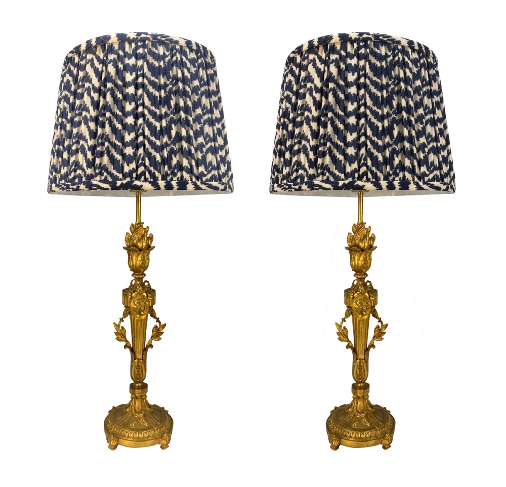A pair of French Louis XVI style gold ormolu candlestick table lamps with gathered blue and cream patterned shades.