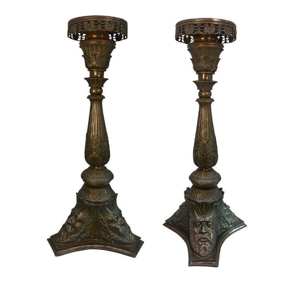 A pair of tall dark bronze Venetian torchere pedestals featuring ornate relief facial masks at the base, leaf-carved columns, and perforated top rims.