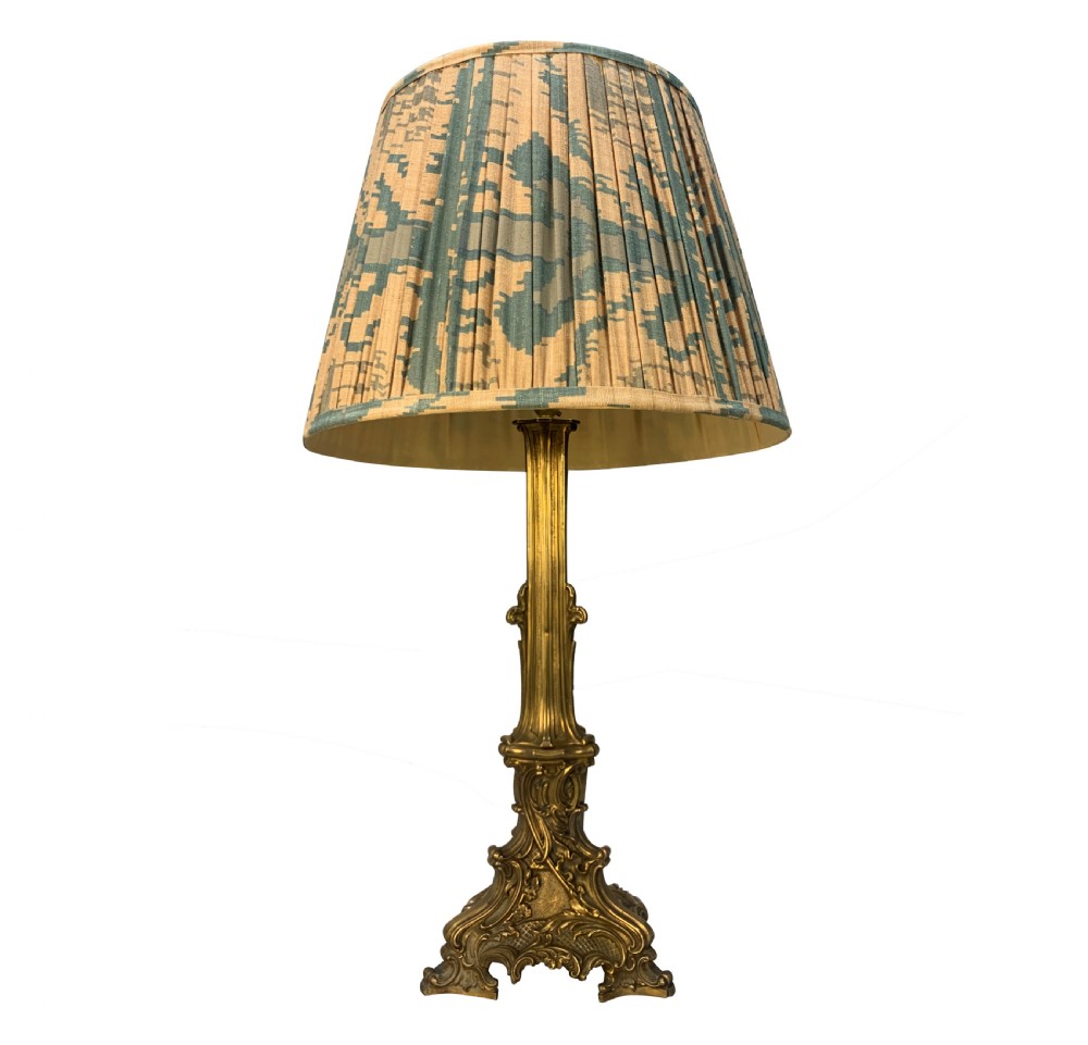 A 19th-century gilt bronze table lamp featuring a fluted column shaft, an ornate scrolled tripod base, and a pleated patterned fabric shade.