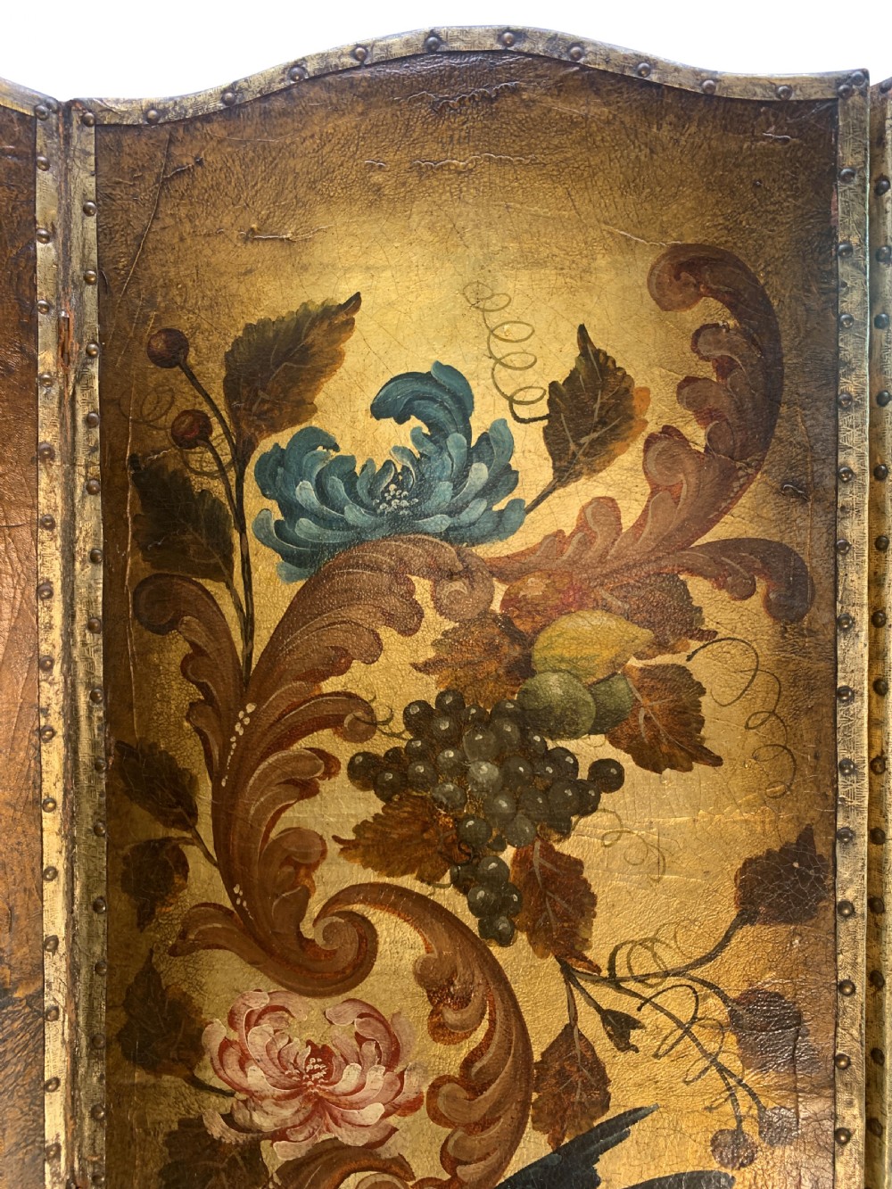 An eighteenth-century four-panel folding screen featuring embossed and hand-painted gilt leather decorated with botanical scrollwork, birds, and fruit, bordered with brass studs. View II