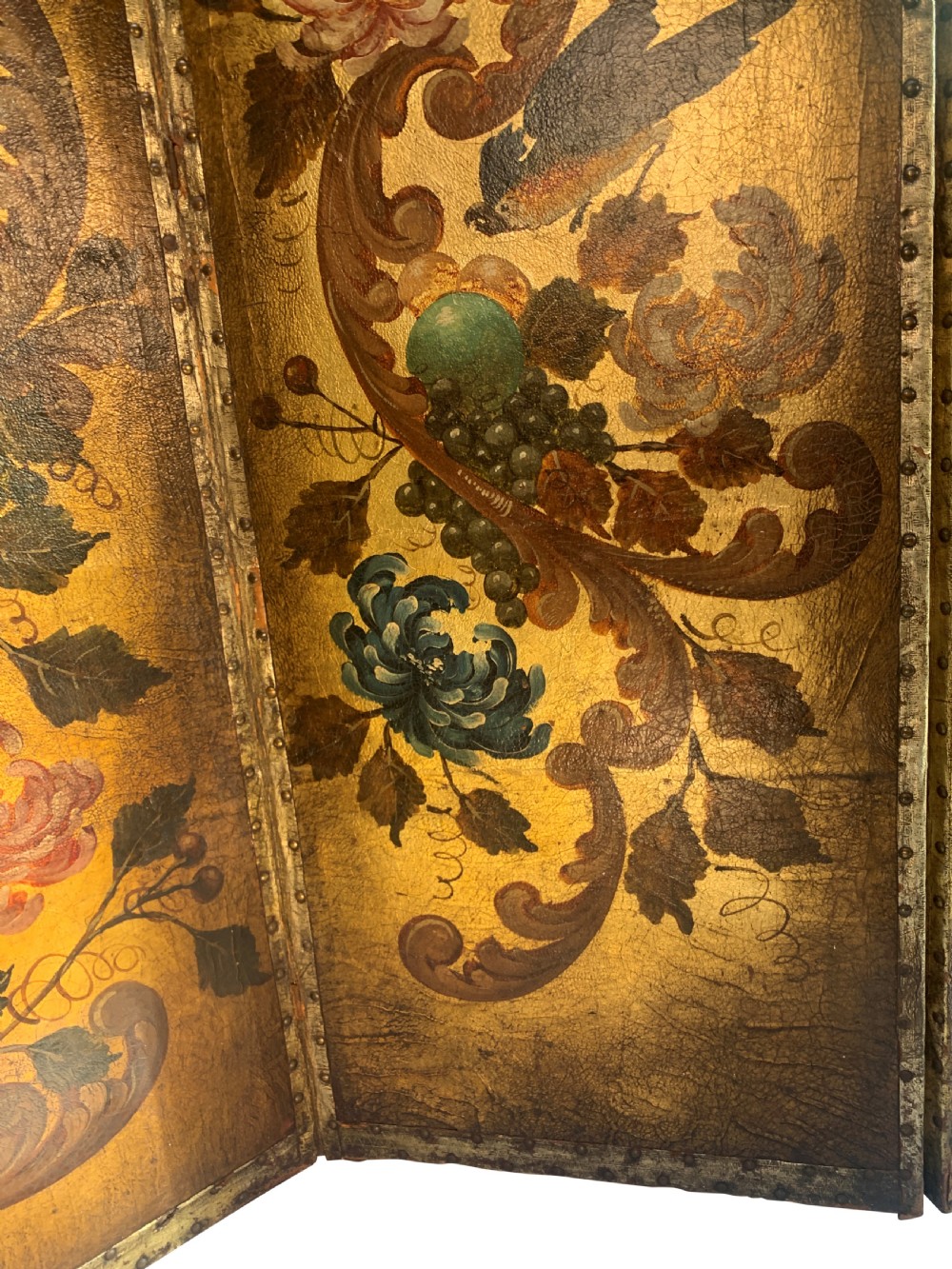 An eighteenth-century four-panel folding screen featuring embossed and hand-painted gilt leather decorated with botanical scrollwork, birds, and fruit, bordered with brass studs. View V