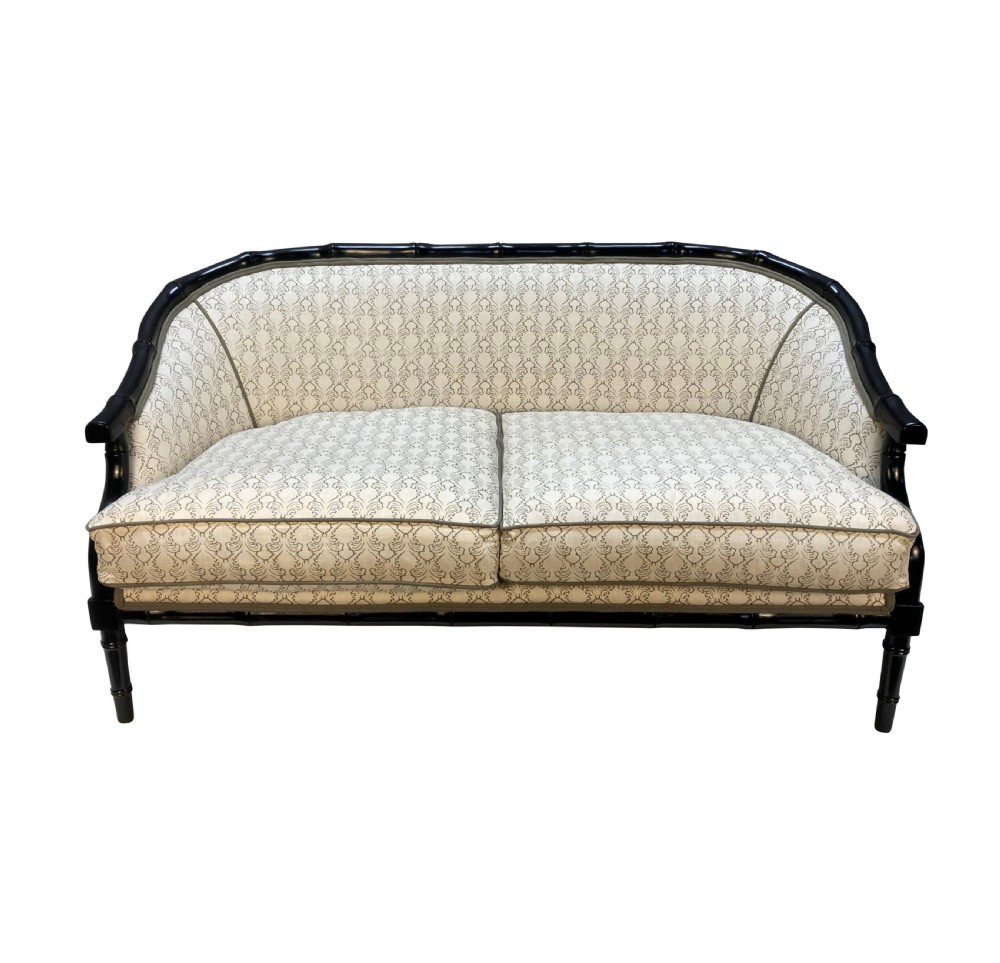 A 1930s French faux bamboo sofa featuring a black lacquered carved frame with a curved back and cream patterned upholstery.