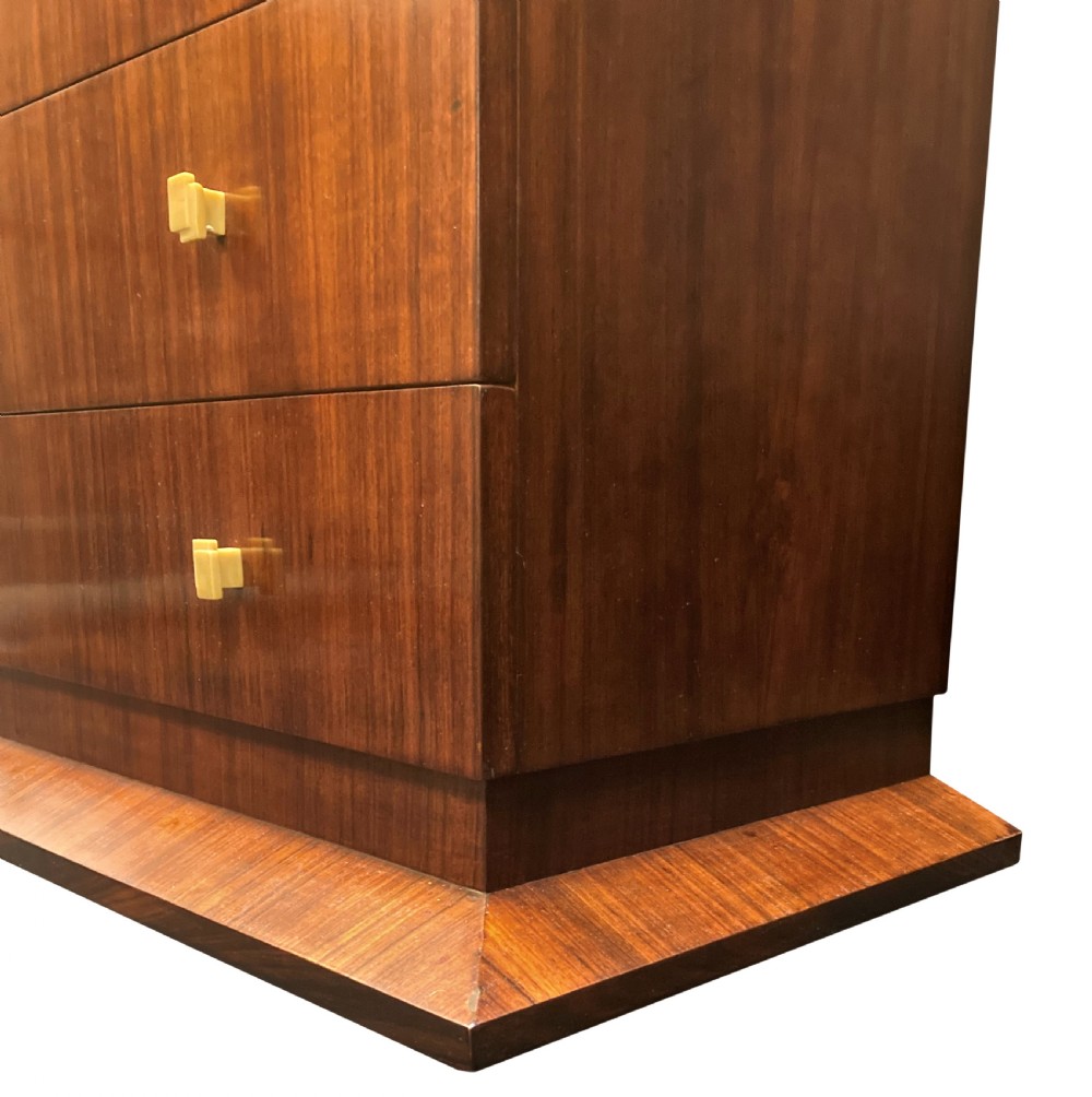 An Art Deco dark wood commode featuring four stacked drawers with cream-coloured Bakelite handles resting on a stepped plinth base. View IV
