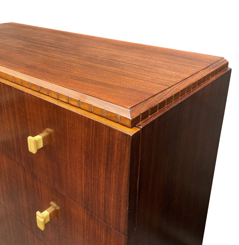 An Art Deco dark wood commode featuring four stacked drawers with cream-coloured Bakelite handles resting on a stepped plinth base. View VI