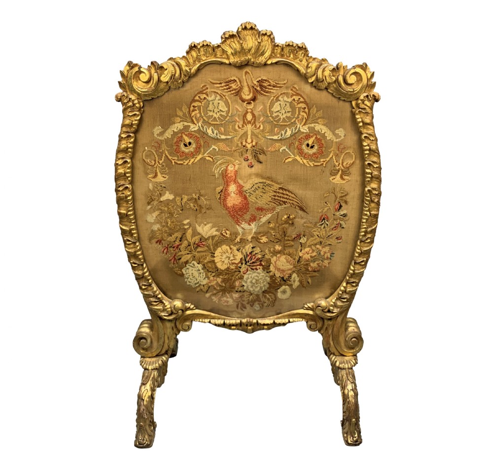 A George III giltwood fire screen with a carved gold frame and a central needlepoint panel depicting a bird and floral motifs.